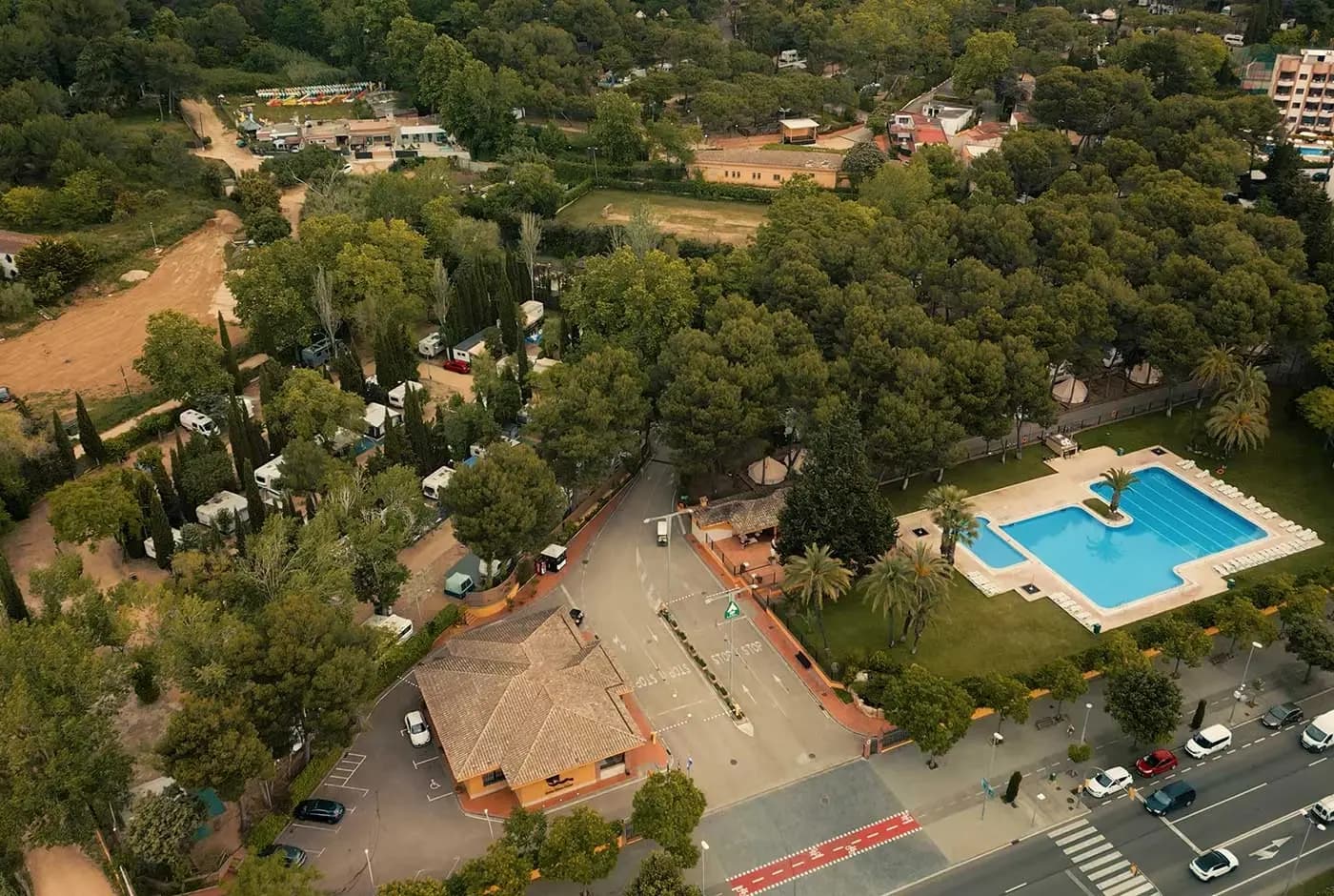 Luchtfoto van de camping in Lloret de Mar, met het zwembad tussen de palmen en plaatsen onder hoge pijnbomen